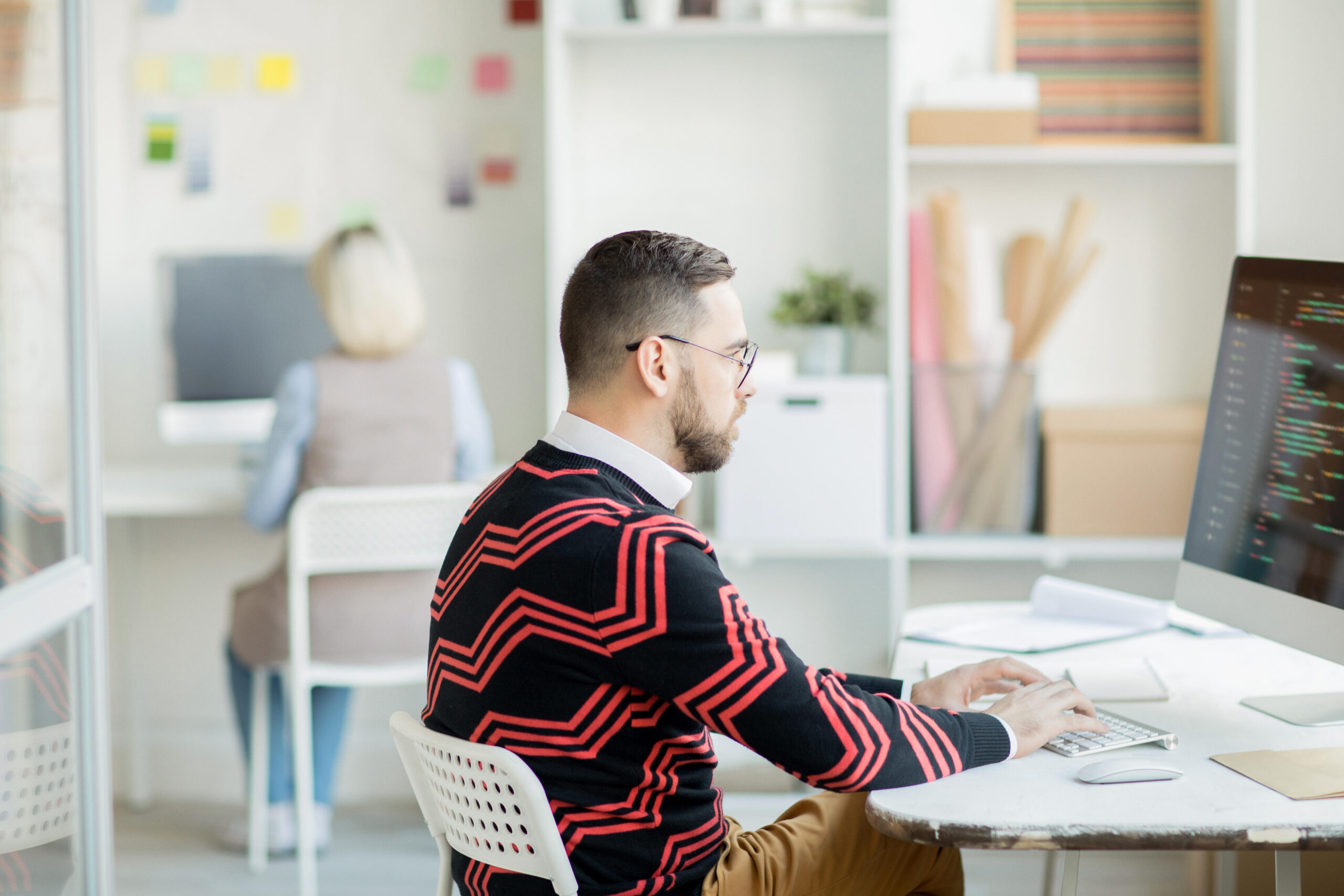 a man and a woman sitting in an office focused on coding wit Zustand
